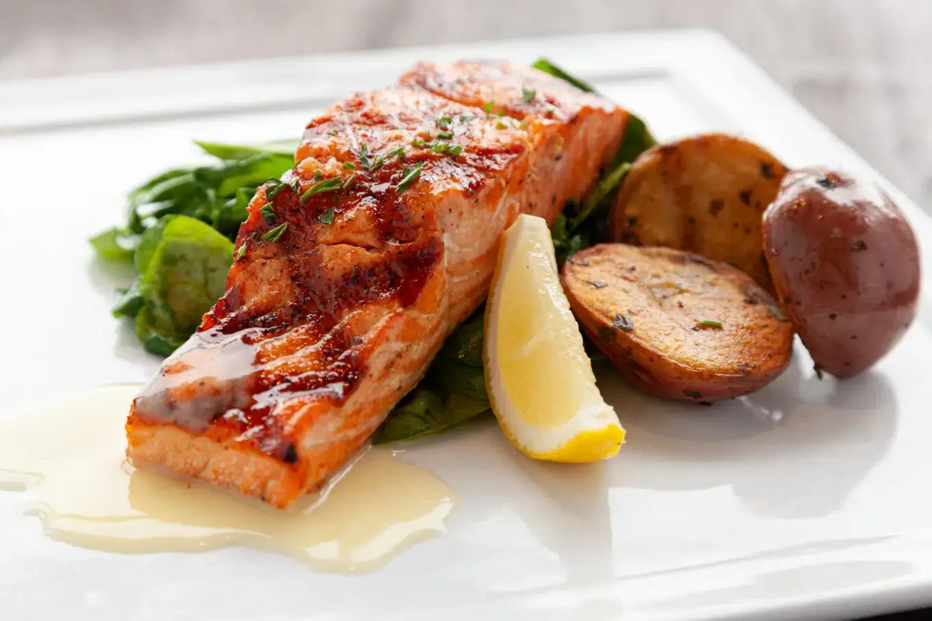 Plank of grilled salmon, new potatoes, greens and lemon wedge.