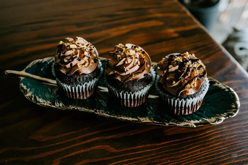 3 Red velvet cupcakes with semi-sweet chocolate chips and sweet cream cheese frosting on top.