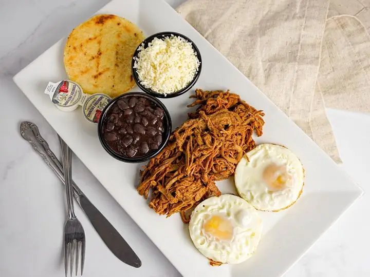 Desayuno Criollo: Arepa, carne mechada, queso rallado, huevos (fritos, revueltos o perico) y frijoles. Arepa, shredded beef, cheese, eggs (scrambled, sunny side or “perico”) and beans.